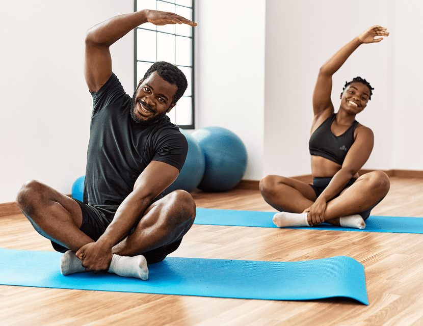 Two people stretching on yoga mats in a bright room.