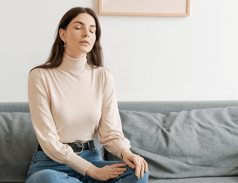 A woman meditates peacefully on a couch in a cozy room.
