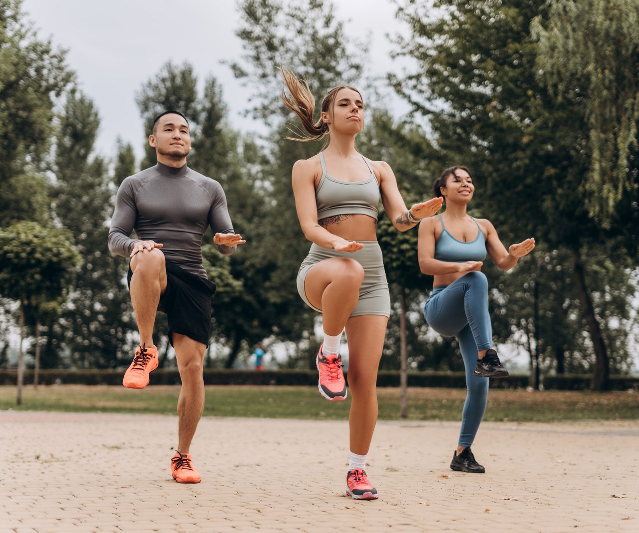 Three people exercising outdoors in a park.