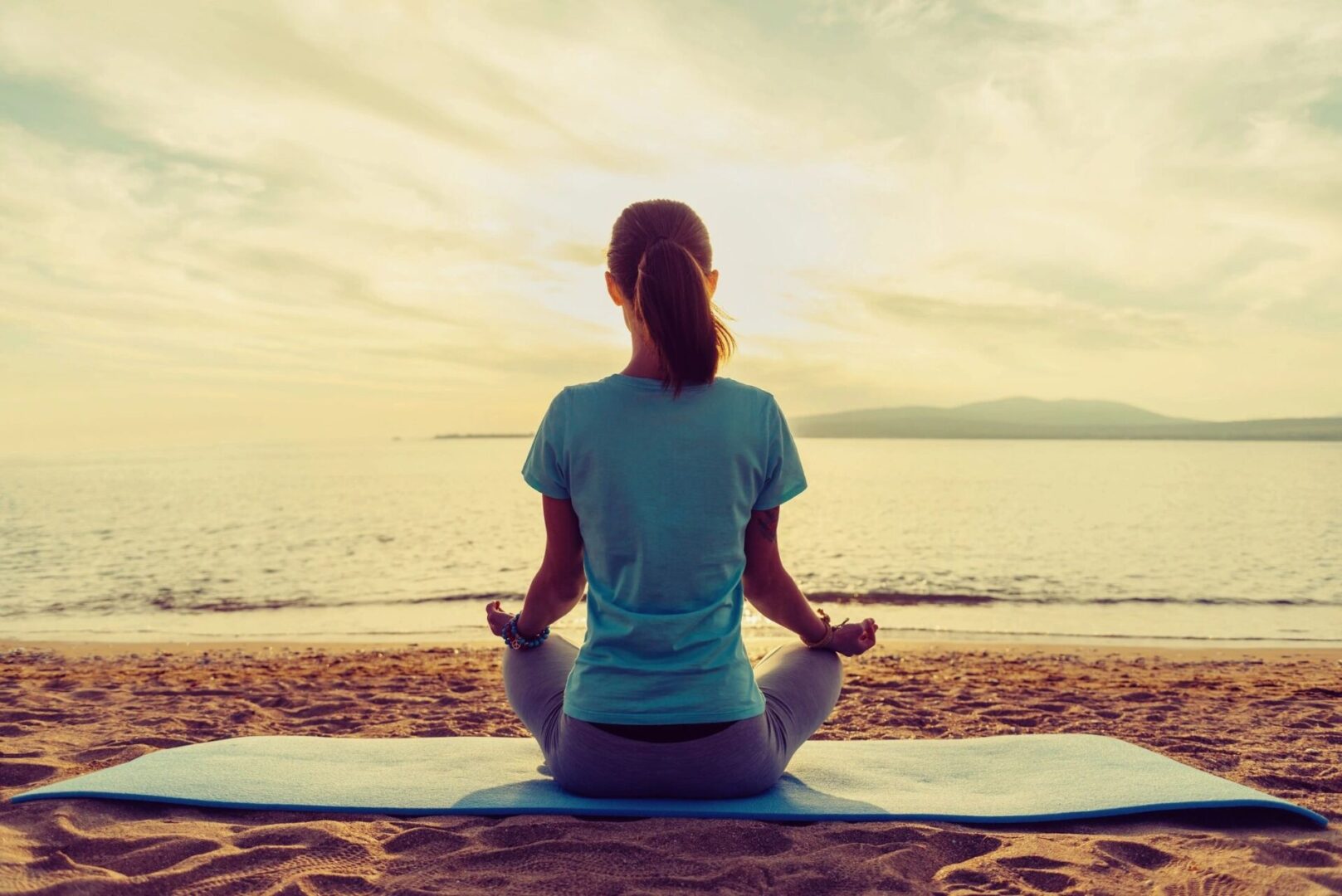 Woman meditating on beach at sunset.