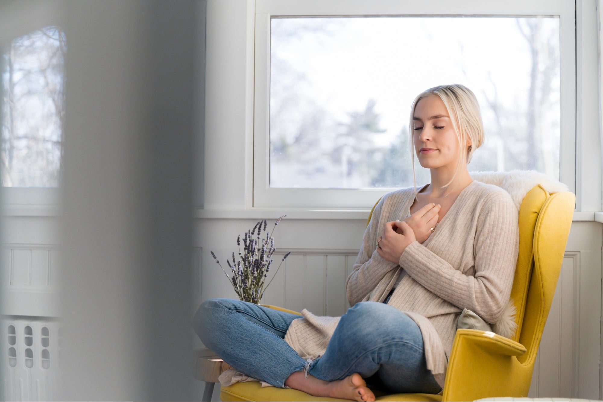 A woman meditates peacefully by a window in a cozy room.