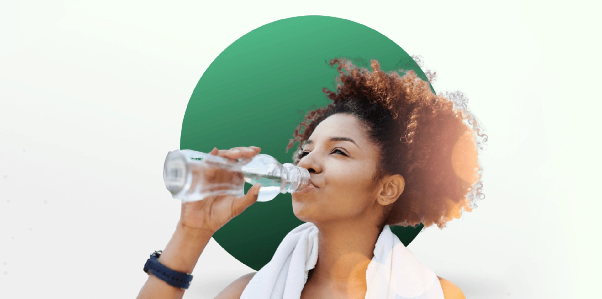 A woman drinks water from a bottle, towel around her neck.