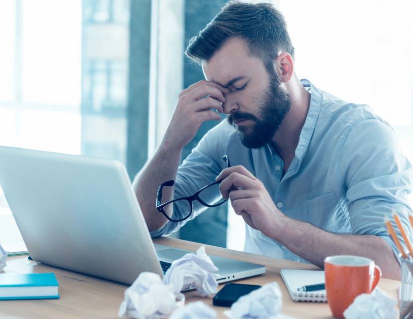 Frustrated man working on a laptop with crumpled papers around.