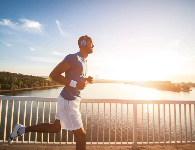 Man jogging on a bridge at sunrise wearing headphones.