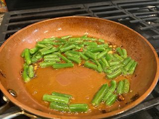 Green beans cooking in a pan with sauce.