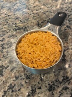 A measuring cup filled with uncooked yellow rice on a countertop.