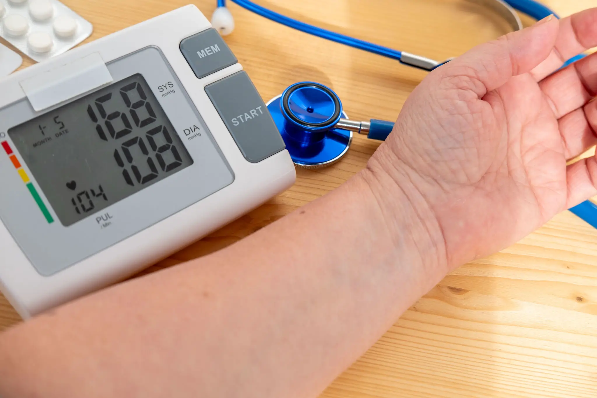 Person measuring blood pressure with a digital monitor and stethoscope.