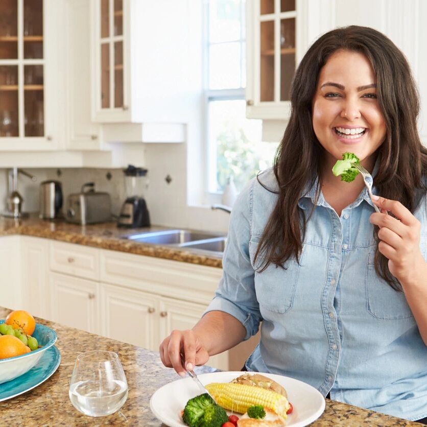 Woman happily eating a healthy meal in a bright kitchen.