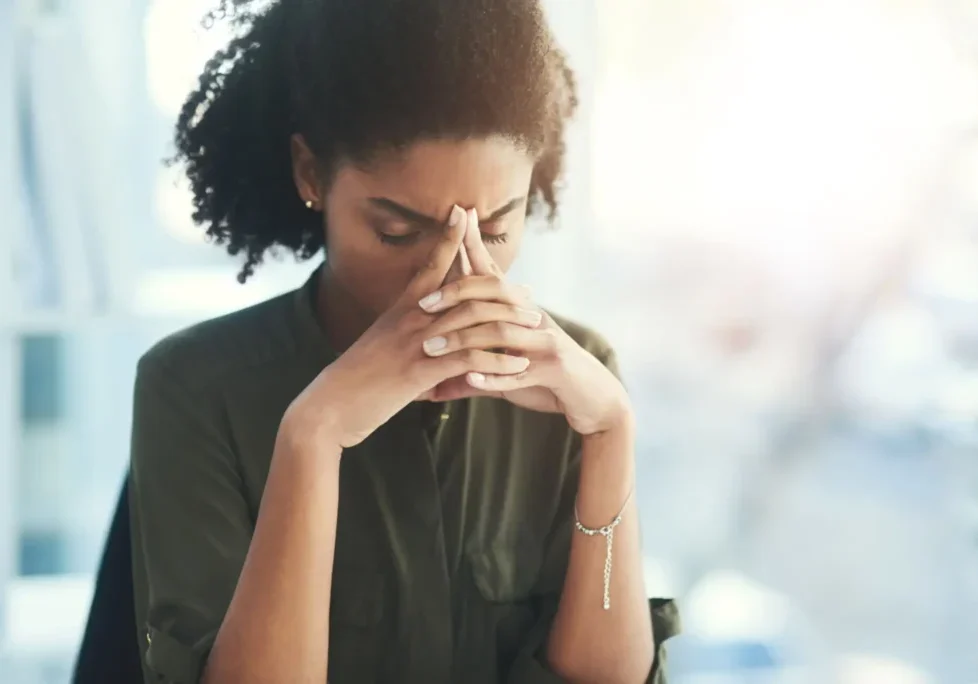 A woman looks stressed and thoughtful with hands clasped near her face.