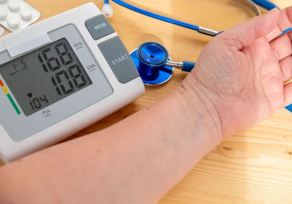 Person measuring blood pressure with a digital monitor and stethoscope.